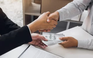 Two people exchanging cash with a handshake, symbolizing a debt settlement agreement.