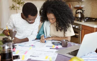 Couple reviewing bills and budget on a laptop in a kitchen.