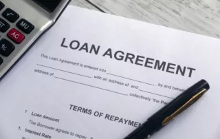 Partially completed loan‑agreement on a wooden desk with a pen and nearby calculator, symbolizing financial planning and the risk to a cosigner in a Michigan bankruptcy case.
